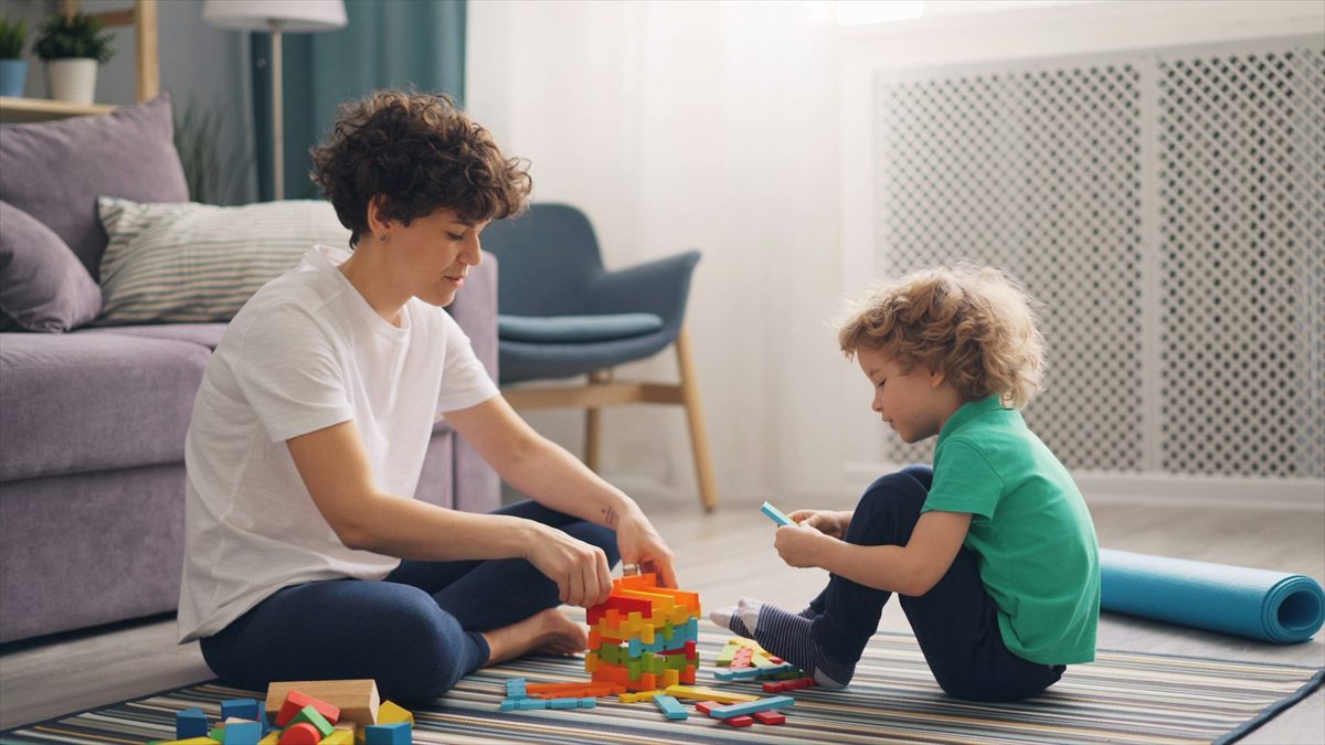 A woman and a young boy playing with colorful building blocks and wooden toys on a striped rug in a living room.